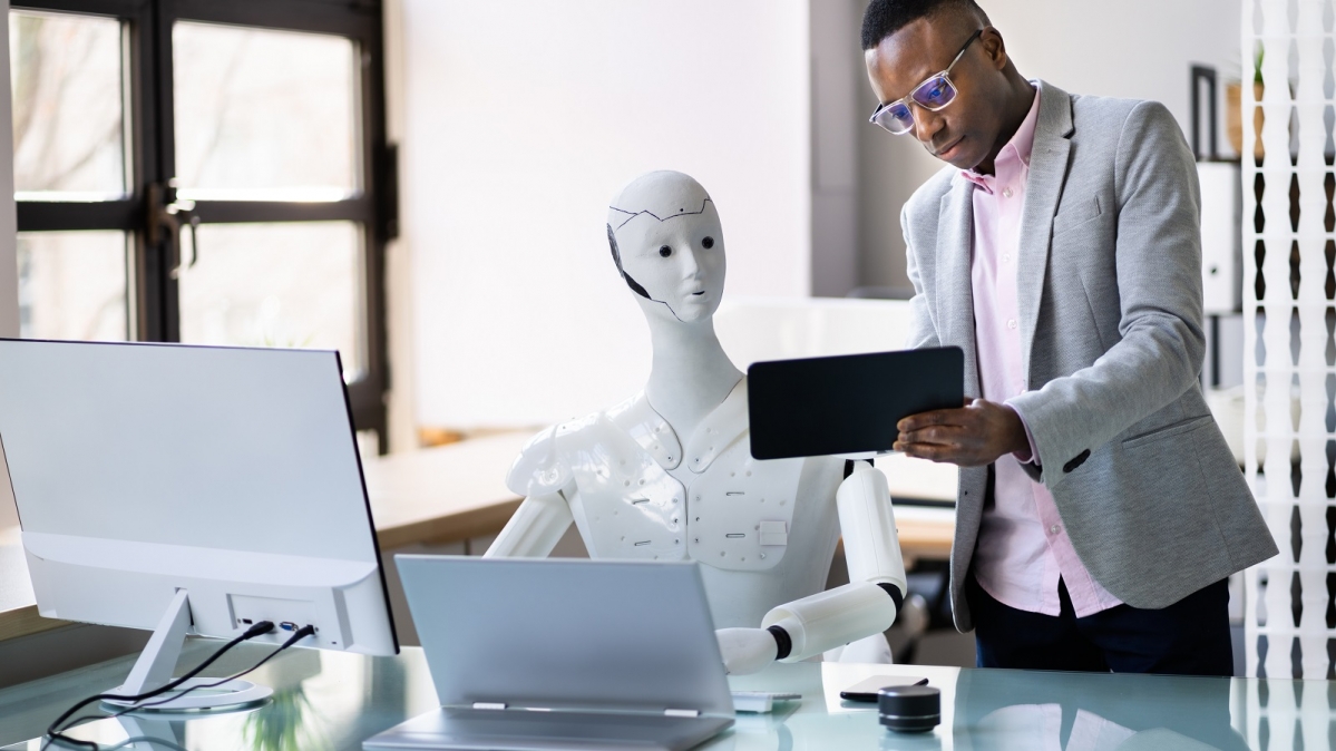 Android und menschlicher Kollege an aenem Bildschirmarbeitsplatz