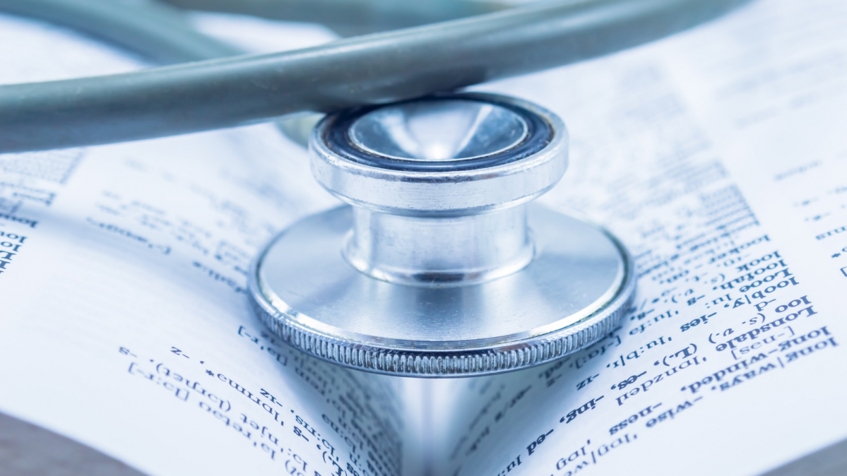 Symbolbild Ärztelatein, geöffnetes medizinisches Wörterbuch und Stethoskop