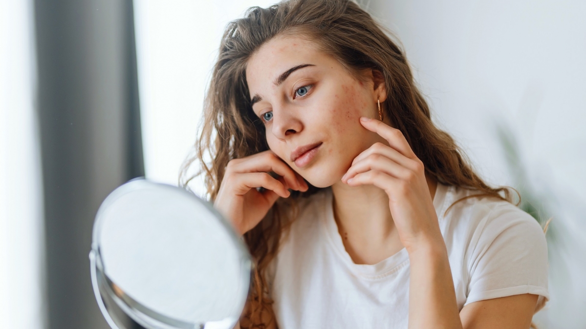 Junge Frau beim Begutachten von Hautunreinheiten im Spiegel