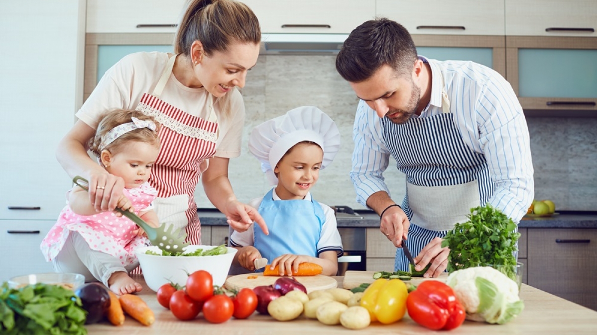 Vater, Mutter und zwei Kleinkinder bei der Essenszubereitung in der Küche