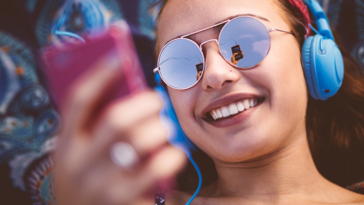  Junge Frau, die über ihre Smartphone Musik konsumiert