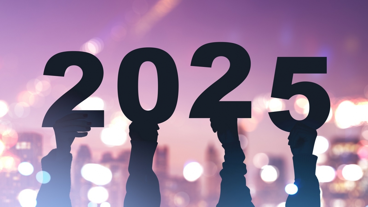 Vier Arme halten die Jahreszahl 2025 empor, nächtlicher Hintergrund mit Bokehlichtern