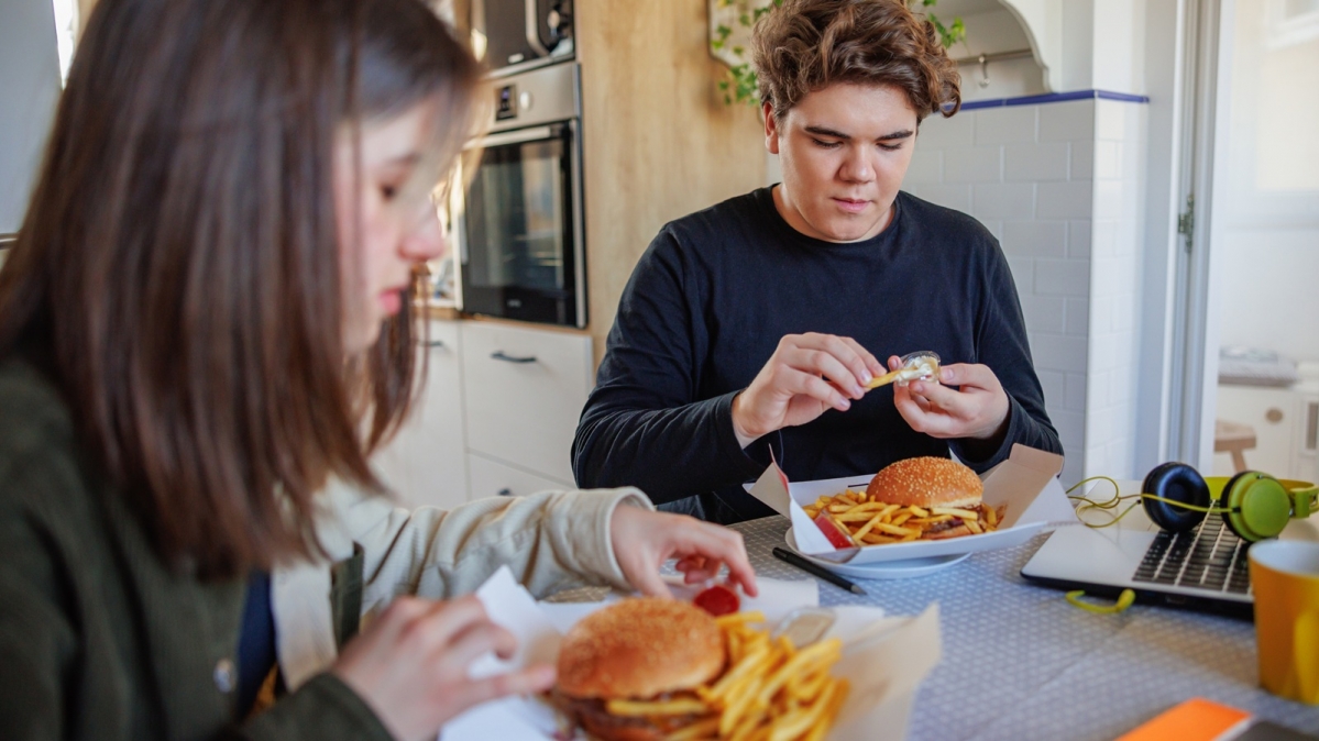 Mädchen und Junge beim Versüiesen eines Burgers mit Pommes Frites