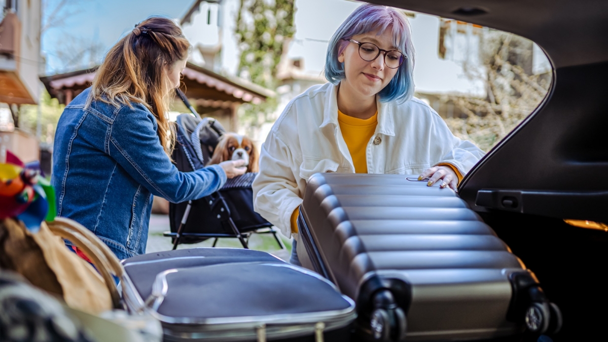 Zwei junge Frauen  beim Verstauen ihres Urlaubsgepäcks im Kofferraum eines PKW
