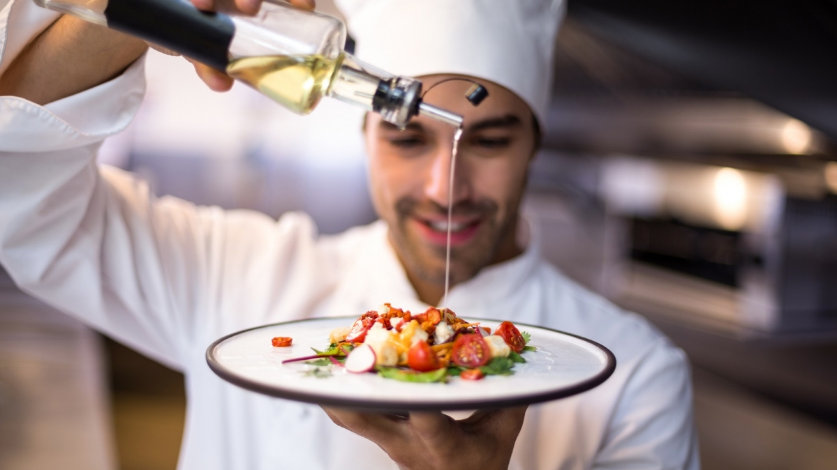 Chef gießt Olivenöl auf Mahlzeit