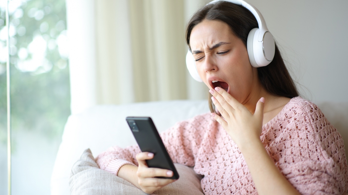 Gähnende junge Frau beim Musikhören per Smartphone