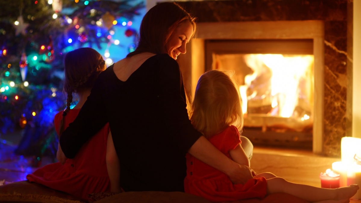 Mutter mit zwei Kindern zu Weihnachten vor einem lodernden Feuer