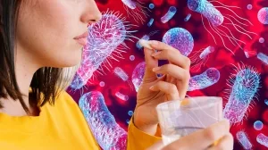 Junge Frau bei der Einnahme eines Anitibiotikums vor einem Hintergrund mit Bakteriendarstellungen