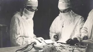 Drei Chirurgen in OP-Kleidung, Masken und Schutzbrillen bei einer Operation.