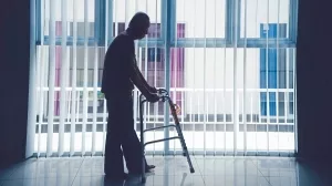 Silhouette_of_lonely_elderly_man_walking_with_a_walker_near_the_window_at_home