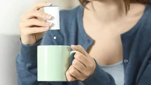 Close_up_of_a_woman_hands_throwing_sacharine_pill_into_a_mug_sitting_on_a_couch_in_the_living_room_at_home
