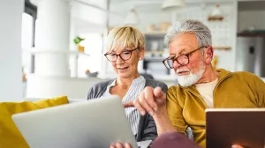 Älteres Paar schaut gemeinsam auf einen Laptop im Wohnzimmer.