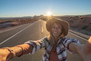 Junge Frau an einem Highway im Monument Valley, Utah, mit Sonnenuntergag im Hintergrund