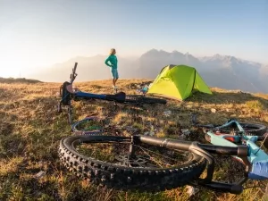 Fahrradreisende neben ihrem Zelt vor einer Gebirgskulisse