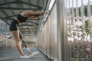 Sportliche junge Frau mit Beinprothese bei Dehnübungen auf einer Brücke
