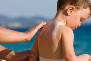 Kleiner Junge erhält am Strand den Rücken mit Sonnencreme eingerieben