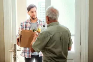 Junger Mann bringt einem älteren Mitbewohner den Einkauf vorbei.