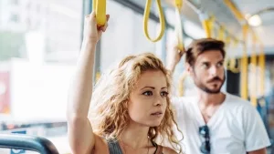 Frau und Mann stehend im Bus, jeweils eine Hand an einer Halteschlaufe