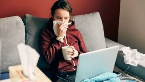 Bettlägerige, erkältete junge Frau mit Laptop auf dem Schoss