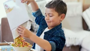 Junge beim  Einfüllen von gesüßten Frühstücksflocken