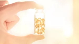 Hand hält Fläschchen mit Vitamin-D-Kapseln ins Sonnenlicht