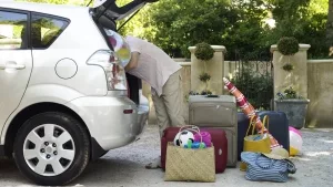 Mann beim Einladen des Urlaubsgepäcks in den Kofferraum eines PKWs