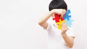 Junge hält sich vier große, verschiedenfarbiige Puzzleteile vors das Gesicht